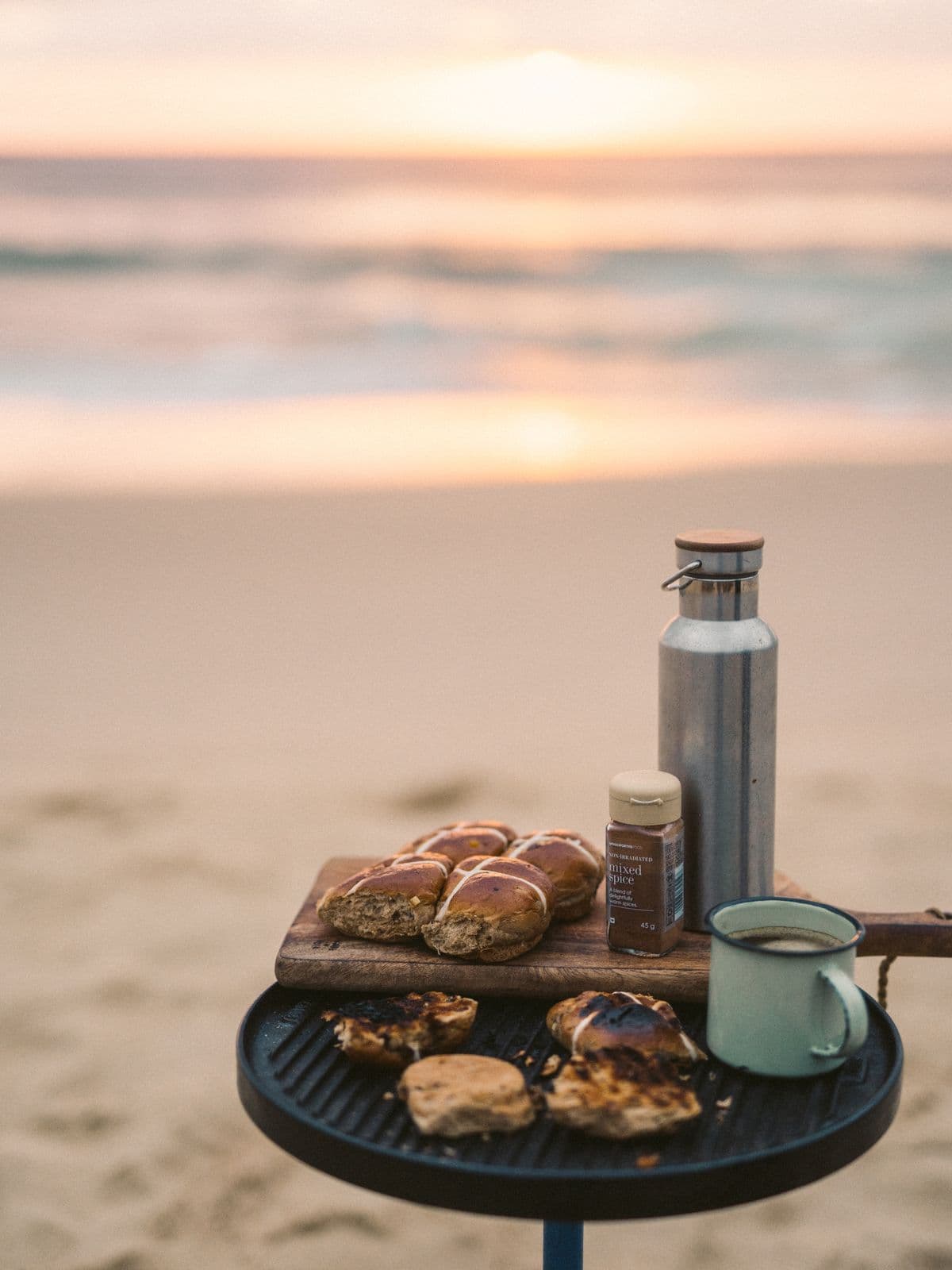Coffee and warm buns on a board, set out on the sand by the sea at sunrise